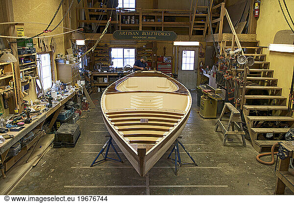 A boat builder  works on the boat he is restoring in a boatbuilding shed.