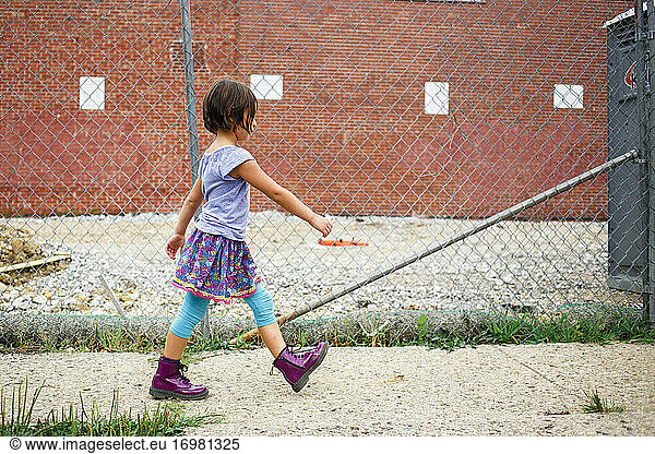 A bold girl in purple boots walks on sidewalk by a construction site