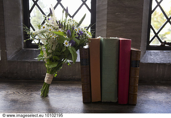 A bouquet of blue and white wedding flowers leaning against books.