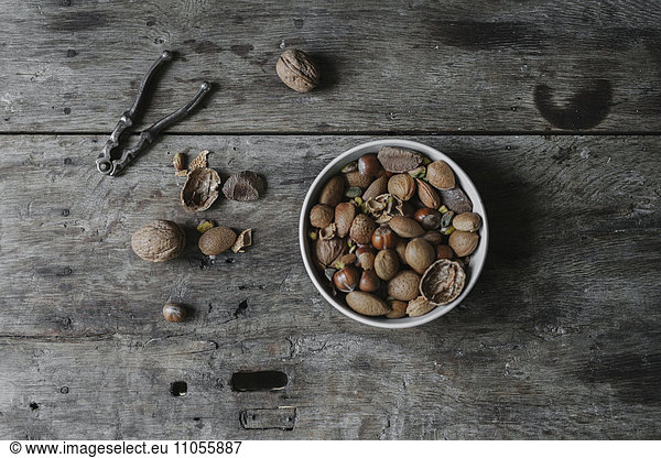 A bowl of mixed nuts  shells and a nutcracker on a table.
