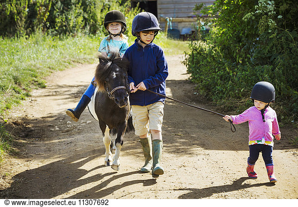 A boy  a toddler  and a girl riding a pony on a dirt path.