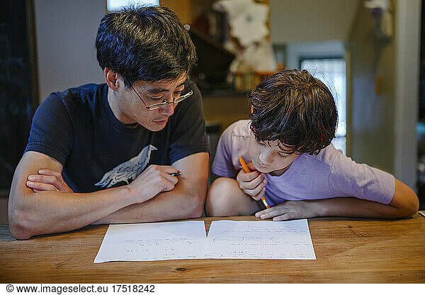 A boy and father sit together at kitchen table doing homework