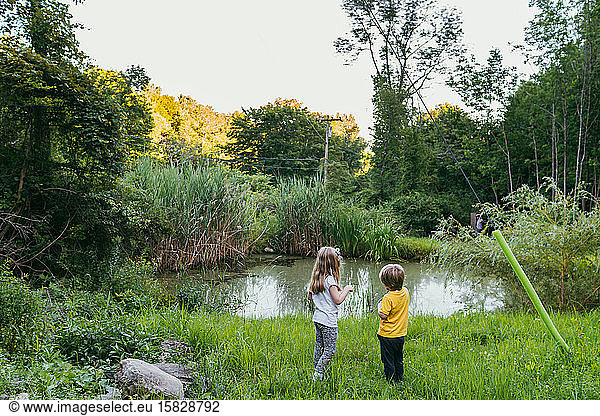 A boy and girl look out at a pond.