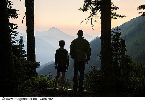 A boy and his dad enjoy the sunset together while camping.