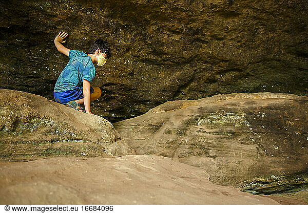 A boy crawls across boulders against rock wall in sandstone gorge