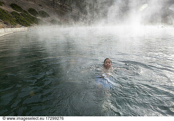 A boy floats in a Trinity Hot Springs pool with steam rising