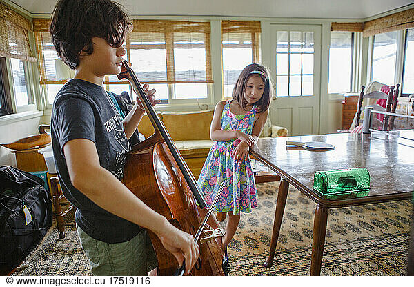 A boy gives cello concert to small mouse in box while sister watches