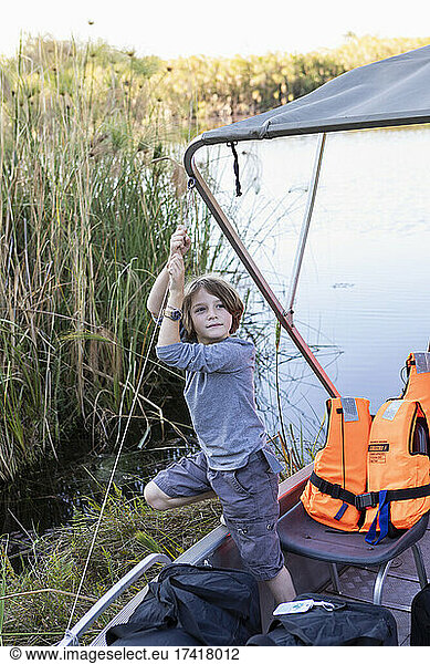 A boy hanging on to the canopy of a small boat on the water of the Okavango Delta