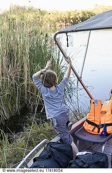A boy hanging on to the canopy of a small boat on the water of the Okavango Delta