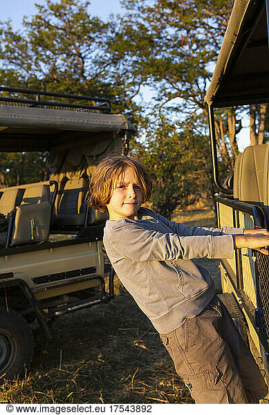A boy hanging on to the side of a stationary jeep looking at the camera.
