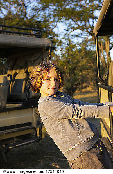 A boy hanging on to the side of a stationary jeep looking at the camera.