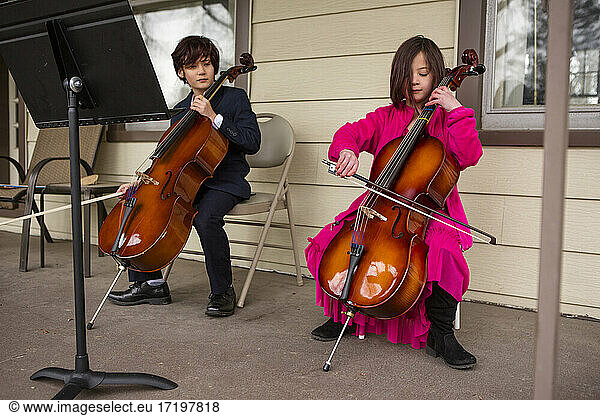 A boy holding cello looks on while his sister plays her instrument