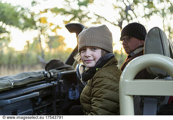 A boy in a hat and coat in a jeep at sunrise on a safari drive.
