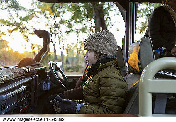 A boy in a hat and coat in a jeep at sunrise on a safari drive.