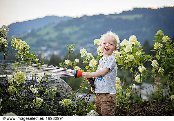 A boy laughing and watering flowers