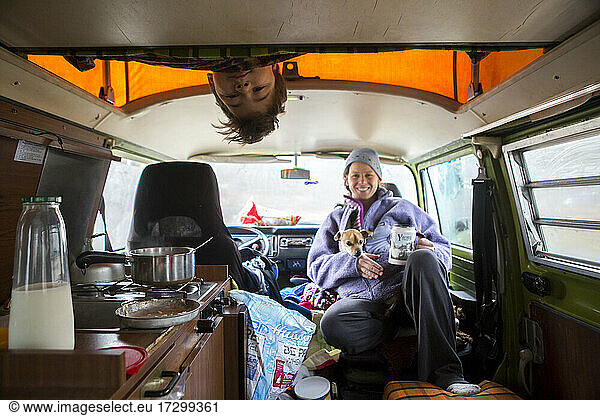 A boy looks down from sleeping loft in VW camper van during road trip.