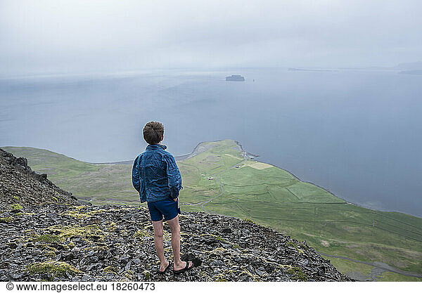 A boy looks out to the Greenland Sea from a mountain top in Iclenad