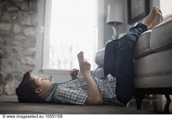 A boy lying on his back on the floor  looking at a digital tablet.