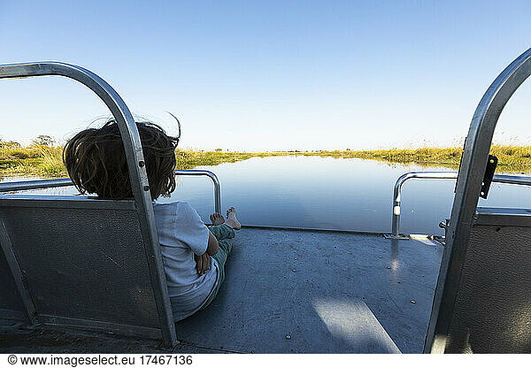 A boy on a motorboat travelling along a waterway in the Okavango delta