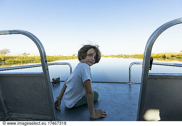 A boy on a motorboat travelling along a waterway in the Okavango delta