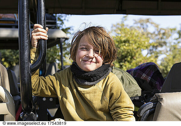 A boy seated in a jeep  smiling  looking at the camera
