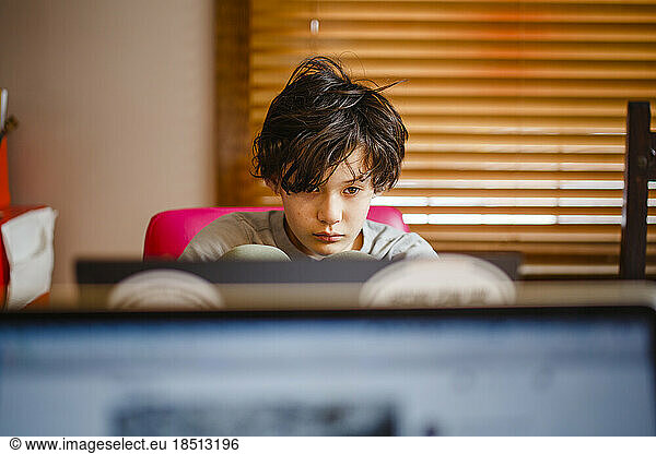 A boy sits at a computer at home working on schoolwork
