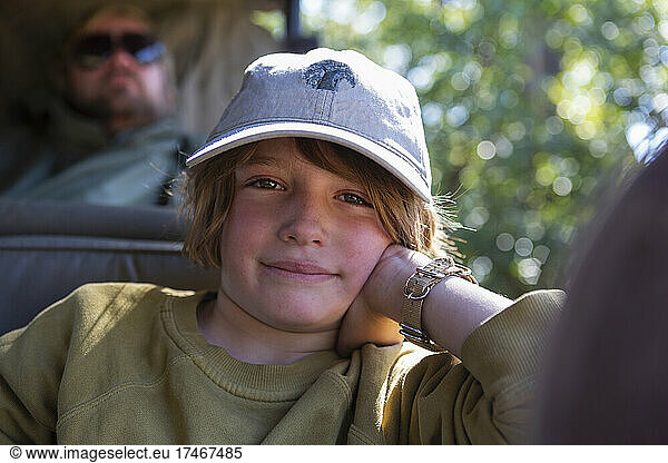 A boy sitting in a jeep leaning on his elbow in a safari jeep.