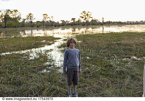 A boy standing alone in an inland delta landscape at sunset.
