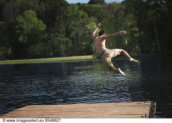 A boy taking a running jump into a calm pool of water  from a wooden jetty.