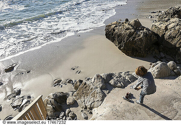 A boy taking his shoes off to go onto a sandy beach