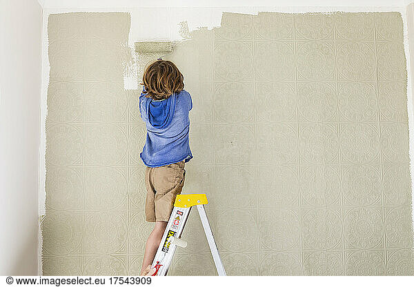 A boy using a paint roller to paint wall