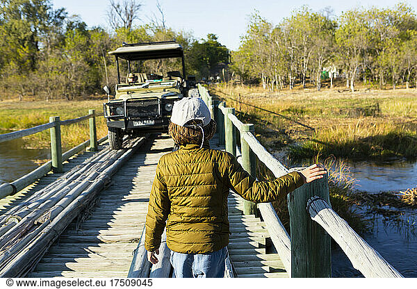 A boy walking across a wooden bridge over marshland.
