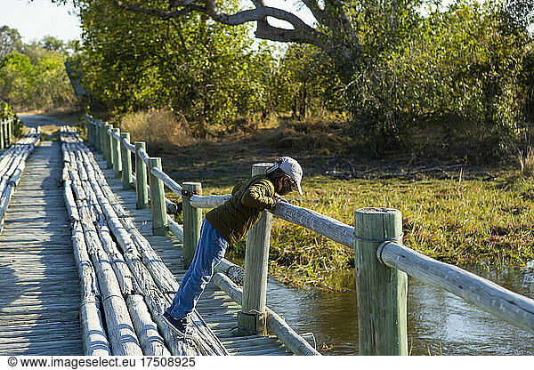 A boy walking across a wooden bridge over marshland alone