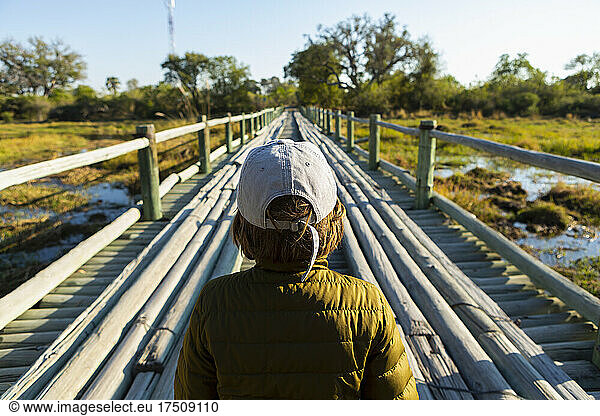 A boy walking across a wooden bridge over marshland alone