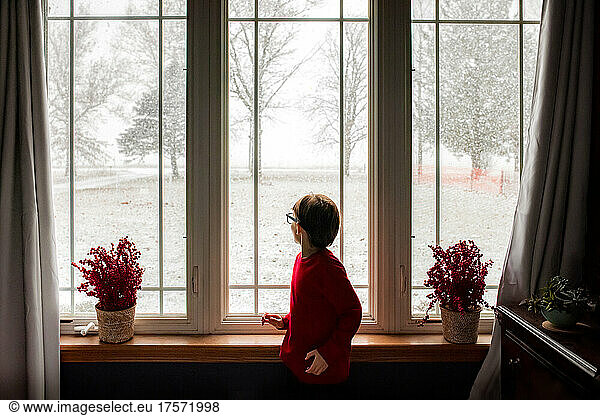 a boy watching the snow fall from his bedroom window