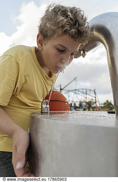 A boy with a basketball drinks water after a workout.