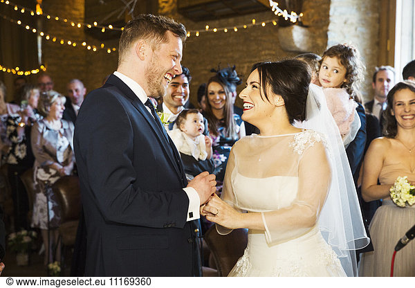 A bride and groom at their wedding ceremony standing side by side in front of the wedding guests.
