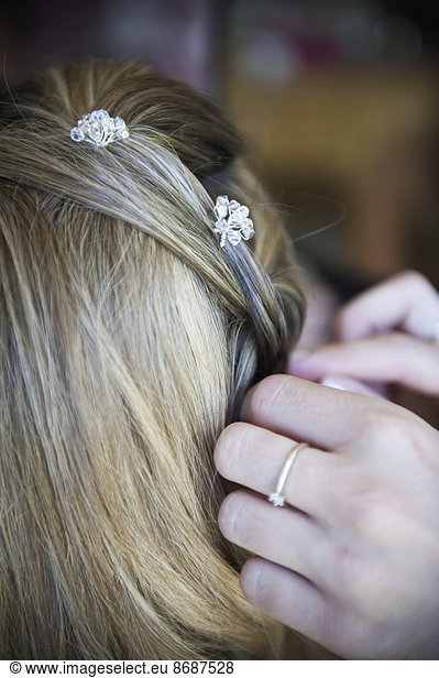 A bride having her hair braided and accessorized with hair pins.