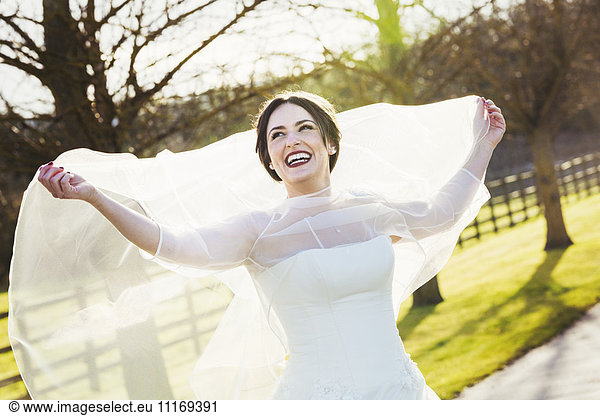 A bride in her wedding dress laughing and holding her veil out behind her  on her wedding day.