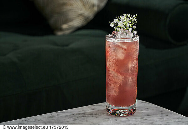 A bright red craft cocktail with flowers for garnish.