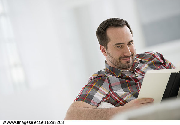 A Bright White Room Interior. A Man Sitting Reading A Book.