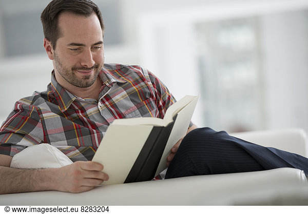 A Bright White Room Interior. A Man Sitting Reading A Book.