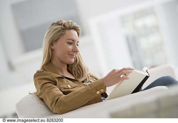 A Bright White Room Interior. A Woman Sitting Reading A Book.