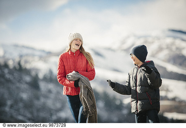 A brother and sister together outdoors in the winter  laughing.