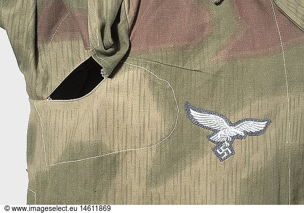 A camouflage jacket of the Luftwaffe Field Division.  Half-long jacket of several fabrics  printed on one side in 'Sumpftarn' (water) camouflage pattern  machine-embroidered breast eagle on blue backing. Metal buttons. No lining  the pockets of brown cotton cloth with RB number and a size stamp. Unworn  fresh colours. historic  historical  1930s  20th century  Air Force  branch of service  branches of service  armed service  armed services  military  militaria  air forces  object  objects  stills  clipping  clippings  cut out  cut-out  cut-outs  uniform  uniforms  clothes  textile  outfit  outfits  wearings  camouflage  camouflages