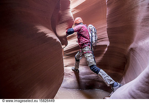 A canyoneer take a big step to avoid deep pothole in slot canyon