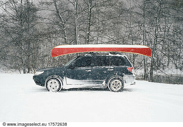 A car with a canadian canoe on the roof by the river in winter.
