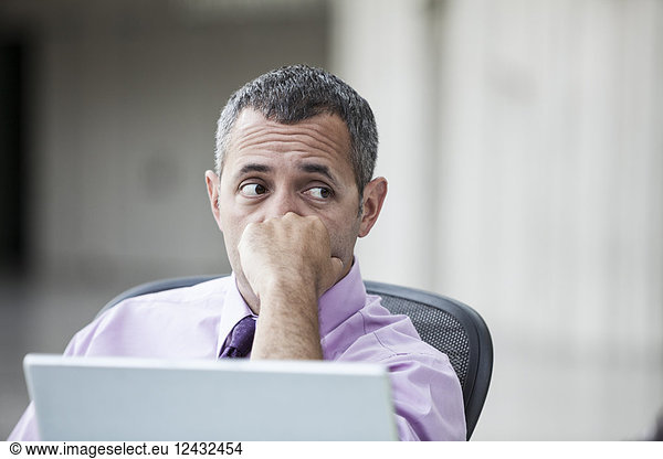 A Caucasian businessman pondering a problem while working on a laptop computer.