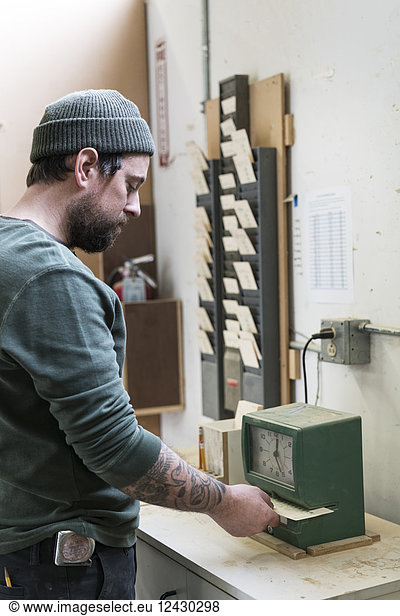A Caucasian carpenter checking in with a time clock in a woodworking factory.