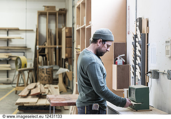 A Caucasian carpenter checking in with a time clock in a woodworking factory.
